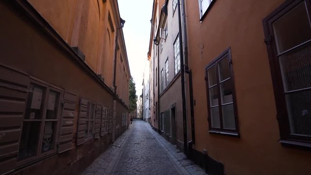 Empty street in the old town of Stockholm Sweden. Steady gimbal footage moving backwards in slow motion. Early summer morning in gamla stan with no people. Old orange houses on a narrow street.