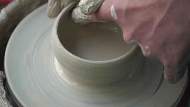 Close up of hands working clay on potter's wheel. Potter shapes the clay product with pottery tools on the potter's wheel