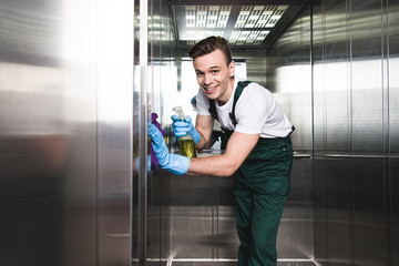 Handsome young cleaning company worker cleaning elevator and smiling at camera