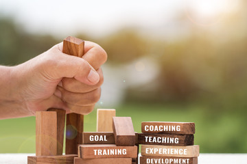 TRAINING business concept : Businessman clasping wooden dominoes square blocks tower in hands feel...