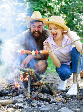 Couple hungry tourists roasting sausages on sticks nature background. Couple in love camping forest roasting sausage at bonfire. Traditional roasted food as attribute of picnic. Camping and picnic