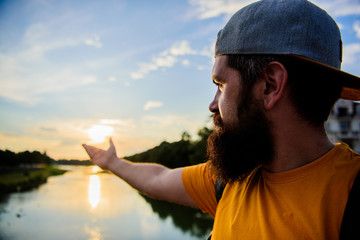 River sun reflection. Man in cap enjoy sunset while stand on bridge. Enjoy pleasant moment. Guy in front of blue sky at evening time admire landscape. Take moment to admire sunset nature beauty