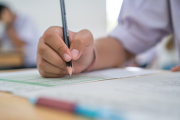 Asian Boy Students taking exams, writing examination room with undergraduate students inside. Student sitting learning lessons on row desk chair doing final exam in classroom with uniform.