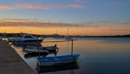 Boats at sunset in mediterranean port under colorful sky and calm waters. Porto Colom, Balearic Islands, Spain