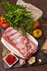Raw pork meat on a slate stone plate with spices, colorful tomatoes and red currant on a wooden rustic background. Top view.