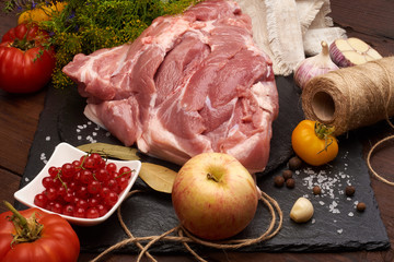 Raw pork meat on a slate stone plate with spices, colorful tomatoes and red currant on a wooden rustic background.