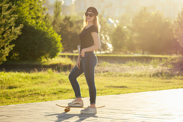 girl skater in a summer park. legs (feet) of woman in fashionable jeans and stylish sneakers on a skateboard (longboard) footway asphalt . youth activity skateboarding concept
