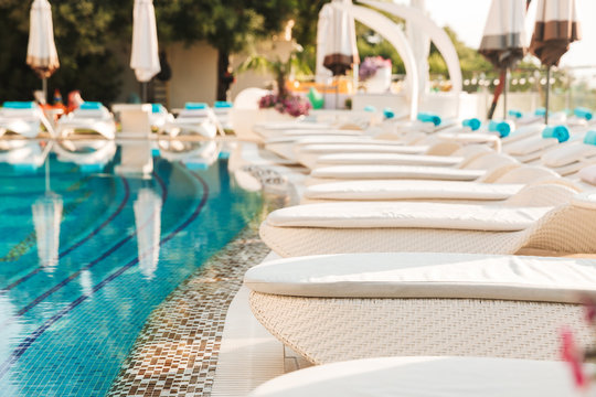 Photo closeup of luxury swimming pool with white fashion deckchairs and umbrellas outdoor near hotel