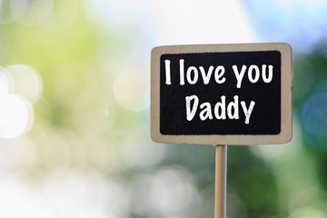 Wooden blackboard label with word I love you Daddy against blurred natural green background for Father's Day concept