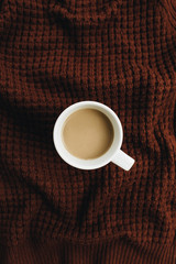 Cup of coffee with milk on brown blanket. Flat lay, top view.