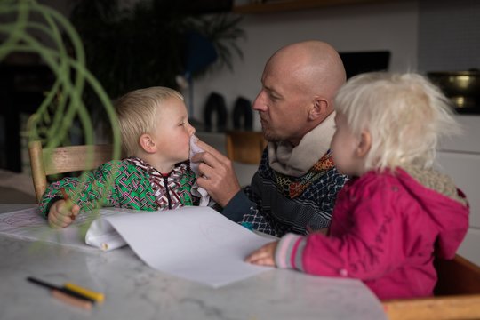 Father cleaning boys mouth in living room