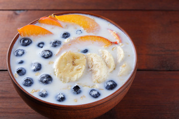 Oatmeal porridge with milk and fruit on wooden background, healthy porridge with pieces of banana and peach, breakfast with fiber, calcium and vitamins