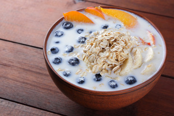 Oatmeal porridge with milk and fruit on wooden background, healthy porridge with pieces of banana and peach, breakfast with fiber, calcium and vitamins