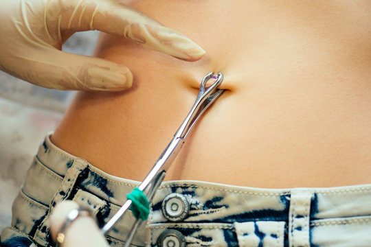 Hand In A Rubber Glove Close-up Of Master Prepares To Pierce The Navel By Belly Of A Young Woman With A Bandage And Cotton On Her Stomach. Care Navel Ring Piercing Concept