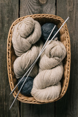 Fototapeta na wymiar top view of beige and grey knitting yarn wit knitting needles in wicker basket on wooden background