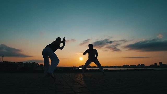 Silhouettes of two sporting men, who dance the Brazilian capoeira on the background of summer sunset
