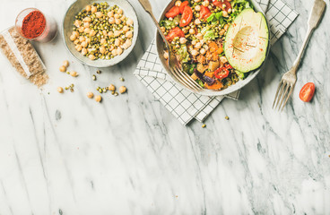 Fototapeta na wymiar Vegan lunch bowl. Flat-lay of dinner with avocado, mixed grains, beans, sprouts, greens and vegetables over marble background, top view, copy space. Clean eating, vegetarian, diet food concept