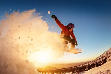 Fototapete Wintersport Snowboarder springt mit Schneestaub in den Sonnenuntergang