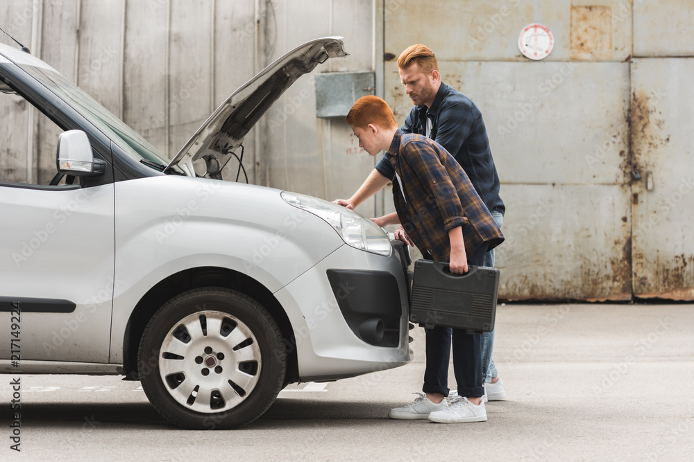 Wall mural side view of father and son repairing car with open hood together