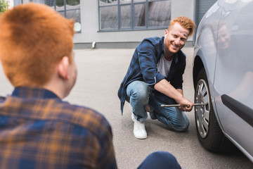 father changing tire in car with wheel wrench and looking at son