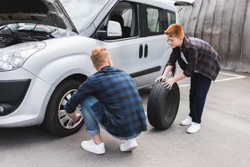 father and son changing tire in car with wheel wrench on weekend