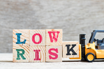 Toy forklift hold letter block K to complete word low risk on wood background