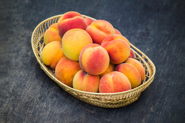 Fresh peaches in wicker basket on dark wood background