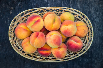 Fresh peaches in wicker basket on dark wood background