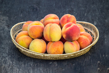 Fresh peaches in wicker basket on dark wood background