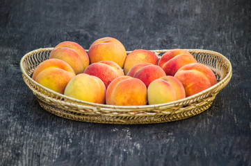 Fresh peaches in wicker basket on dark wood background