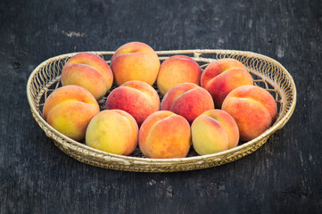 Fresh peaches in wicker basket on dark wood background