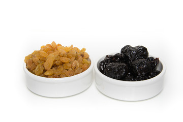 Bowls of raisins and prunes on white background
