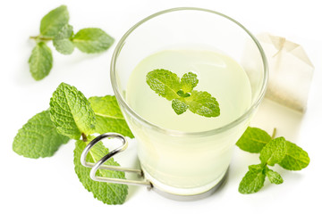 glass of hot tea and mint leaves on white background