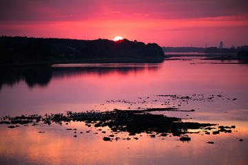 Naklejka premium Bright, colorful evening landscape over the river Daugava of pink and purple tones. Dramatic sunset scenery in Latvia, Northern Europe.