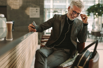 Mature businessman at cafe listening music from cellphone