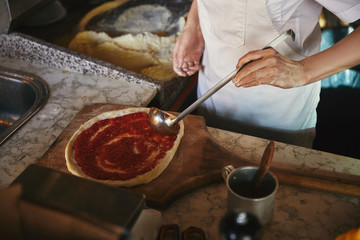 cropped shot of chef pouring ketchup onto pizza dough at restaurant kitchen