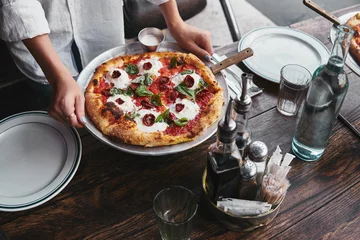 Fototapeten cropped shot of woman carrying plate with pizza margherita to serve on table at restaurant © LIGHTFIELD STUDIOS