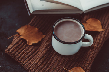 A cup of warm coffee and a book on a knitted scarf. Comfort. Autumn. Cozy weekend