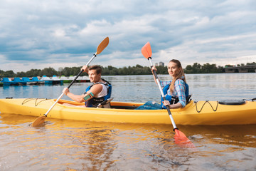 Yellow canoe. Handsome blue-eyed trainer and appealing woman sitting in yellow canoe having river ride