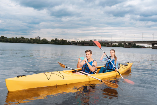 Picture of landscape. Handsome man sitting in kayak with his beautiful woman taking picture of nice landscape