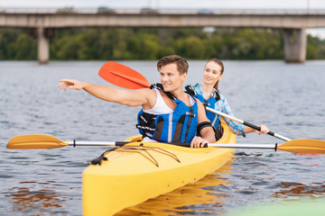 Correct direction. Handsome blonde-haired trainer showing beautiful woman sitting in canoe correct direction