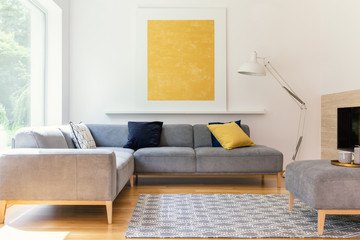 Yellow painting and lamp in modern living room interior with grey corner sofa. Real photo