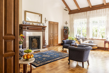 Blue armchairs and patterned carpet in front of wooden fireplace in sophisticated interior. Real photo