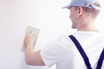 Home interior renovation handyman smoothing down a white wall with a sandpaper tool