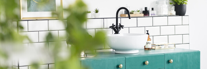 Real photo with blurred foreground of white bathroom interior with tiles, fresh plants and sink on...