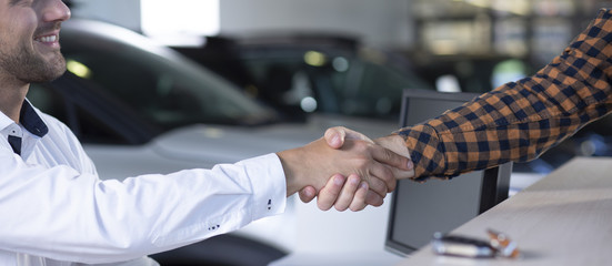 Panorama of smiling car dealer shaking hand with buyer in the salon