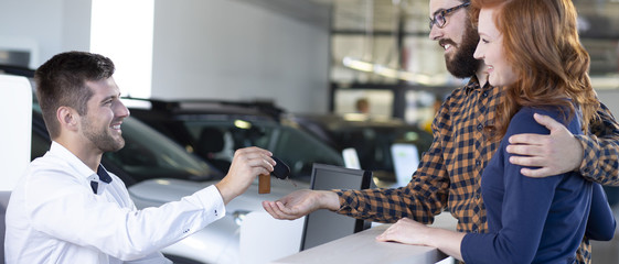 Professional car seller giving keys to happy marriage in the showroom