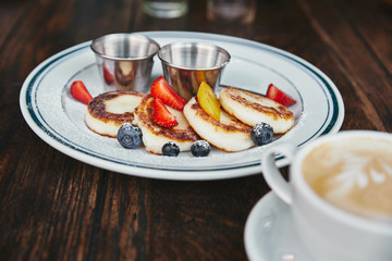 delicious syrniki on plate and cup of coffee on rustic wooden table