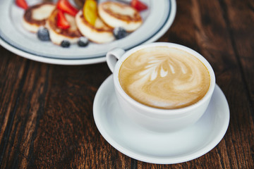 close-up shot of tasty cheese pancakes on plate and cup of coffee on rustic wooden table