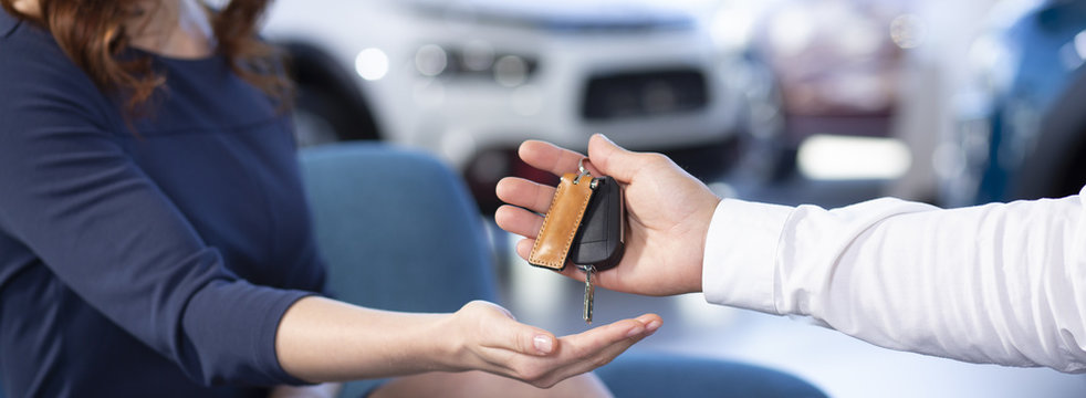 Panorama and close-up of car dealer's hand giving keys to buyer